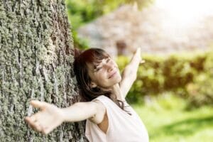 Kobieta obejmuje drzewo w parku, co ilustruje naturalne sposoby na stres.